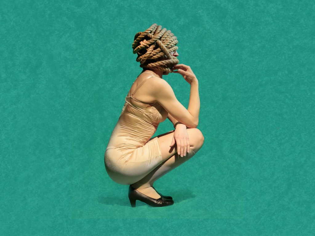 Medusan huone -näytelmän mainoskuva. Alushameeseen pukeutunut nainen istuu sivuttain kyykyssä päässään manillaköydestä muotoiltu kampaus.